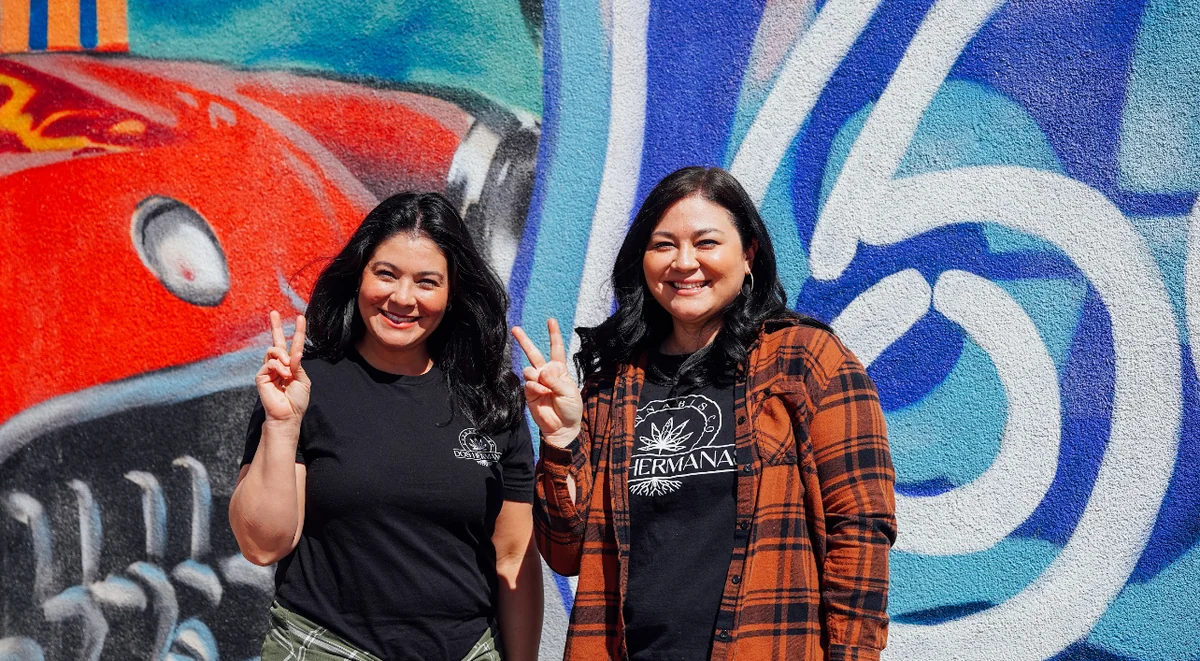 The two sisters who founded Dos Hermanas Canna Co in front of a Route 66 mural in Santa Rosa, New Mexico